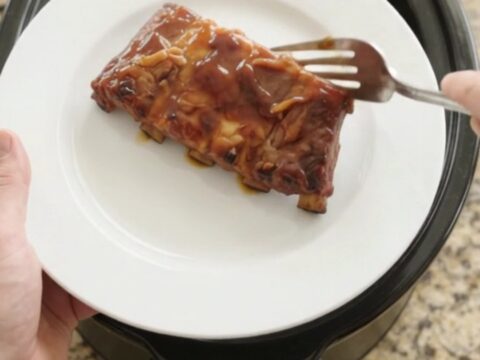 Slow cooker cherry cola honey hickory spare ribs, glistening with a dark glaze, on a white plate.