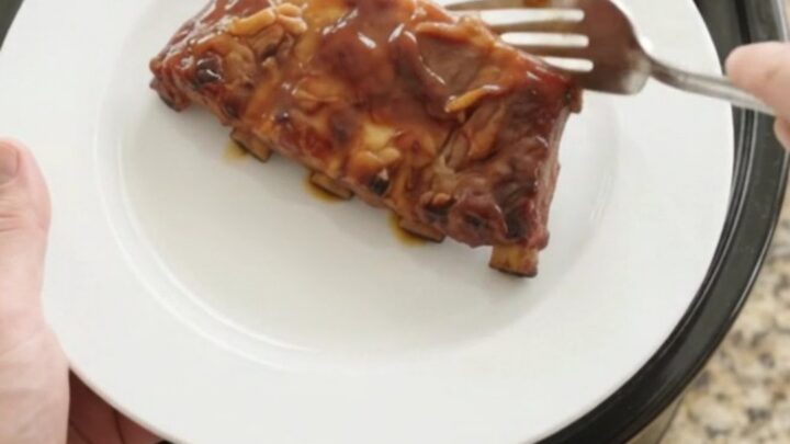 Slow cooker cherry cola honey hickory spare ribs, glistening with a dark glaze, on a white plate.