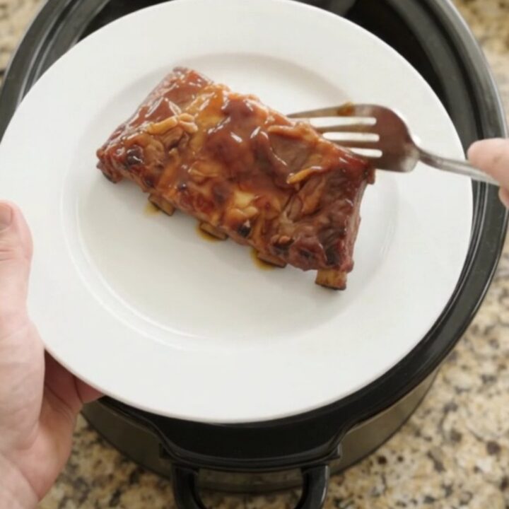 Slow cooker cherry cola honey hickory spare ribs, glistening with a dark glaze, on a white plate.