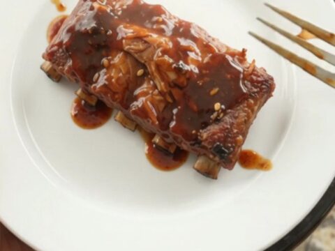Slow-cooker spare ribs glazed with molasses BBQ sauce, garnished with fresh herbs