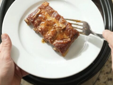 Slow cooker spare ribs glazed with maple bourbon BBQ sauce and caramelized Vidalia onions, shown in the crockpot.