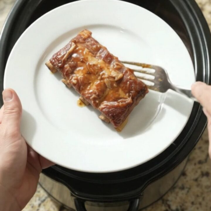 Slow cooker spare ribs glazed with maple bourbon BBQ sauce and caramelized Vidalia onions, shown in the crockpot.