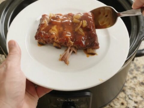 Root Beer BBQ Spare Ribs in slow cooker, glistening with sticky sauce and topped with caramelized onions.