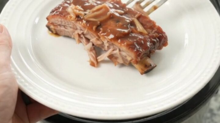 Slow cooker full of glazed spare ribs with caramelized onions and sauce