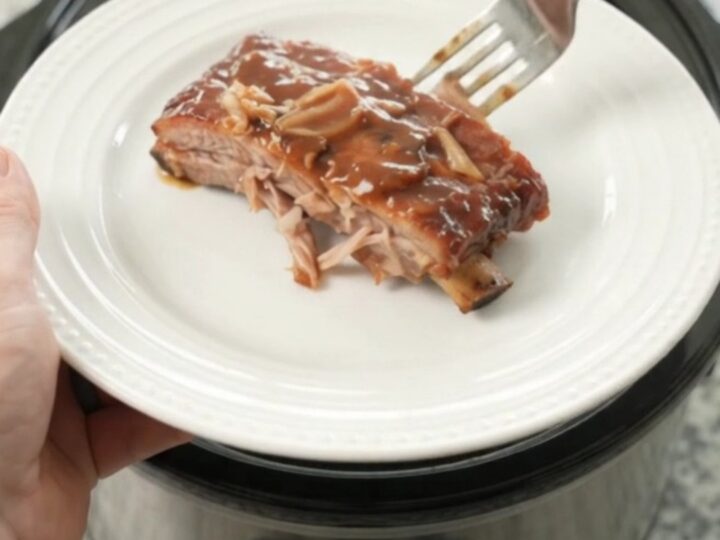 Slow cooker full of glazed spare ribs with caramelized onions and sauce