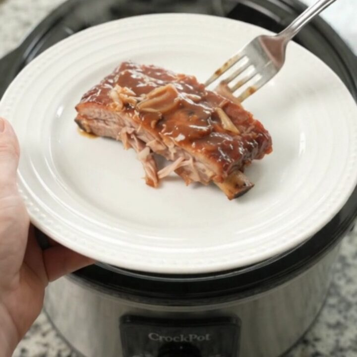 Slow cooker full of glazed spare ribs with caramelized onions and sauce