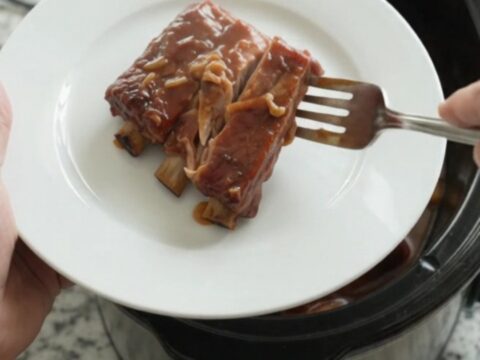 Slow cooker full of glistening spare ribs in BBQ sauce with caramelized onions