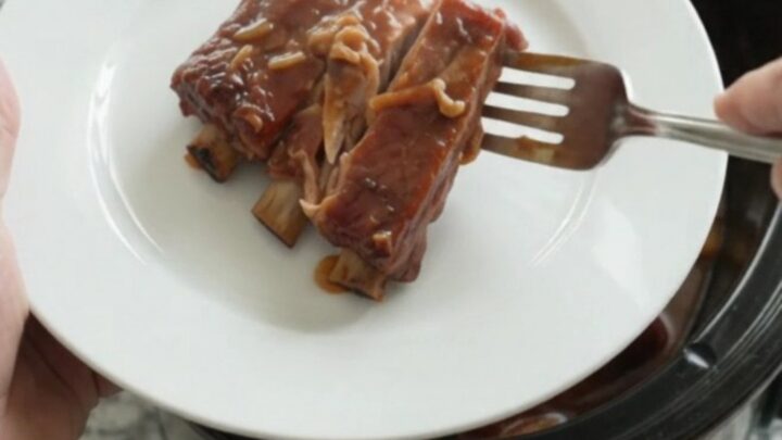 Slow cooker full of glistening spare ribs in BBQ sauce with caramelized onions