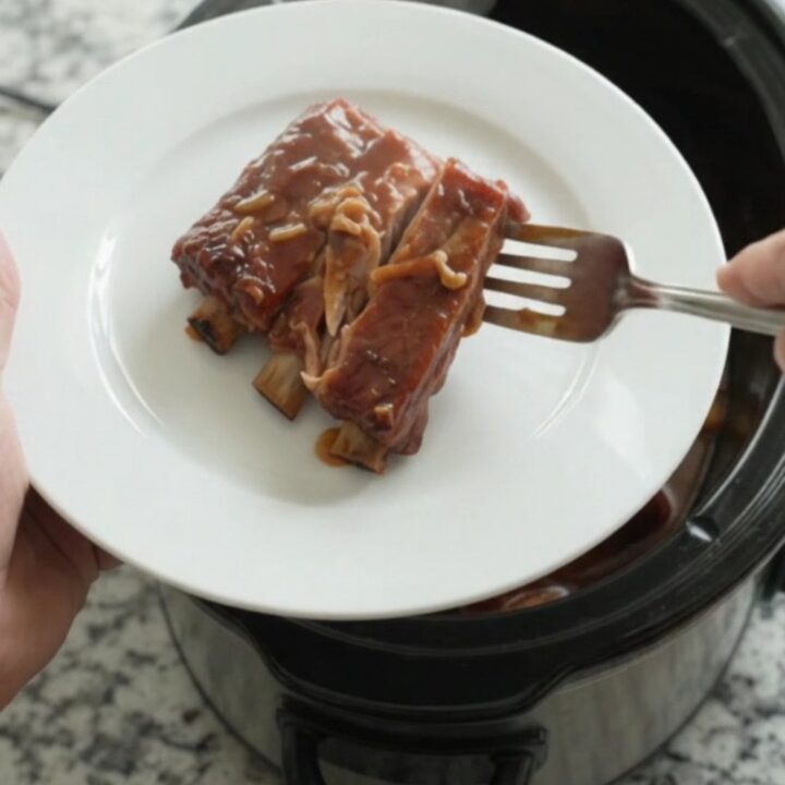 Slow cooker full of glistening spare ribs in BBQ sauce with caramelized onions