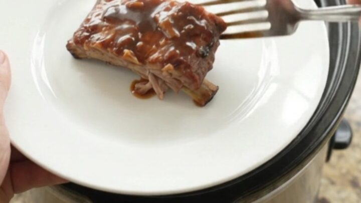Slow cooker full of glazed spare ribs with onions and sauce