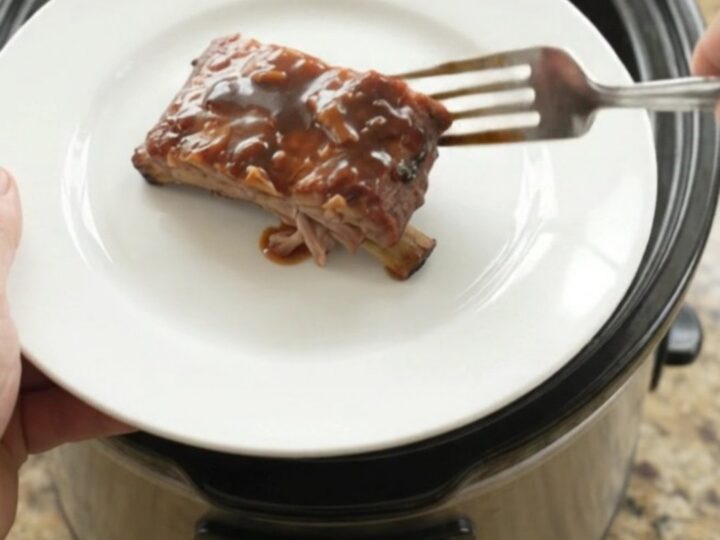 Slow cooker full of glazed spare ribs with onions and sauce
