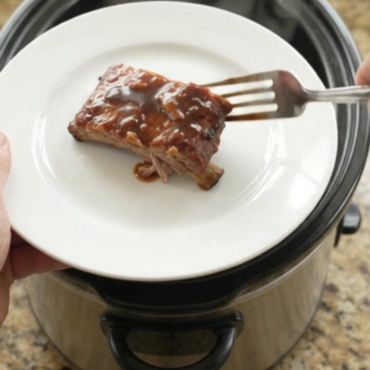 Slow cooker full of glazed spare ribs with onions and sauce