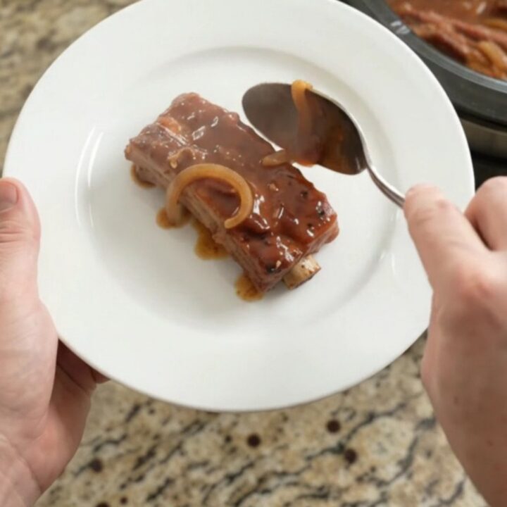 Fork-tender brown sugar BBQ country pork ribs glistening in a slow cooker with caramelized onions.
