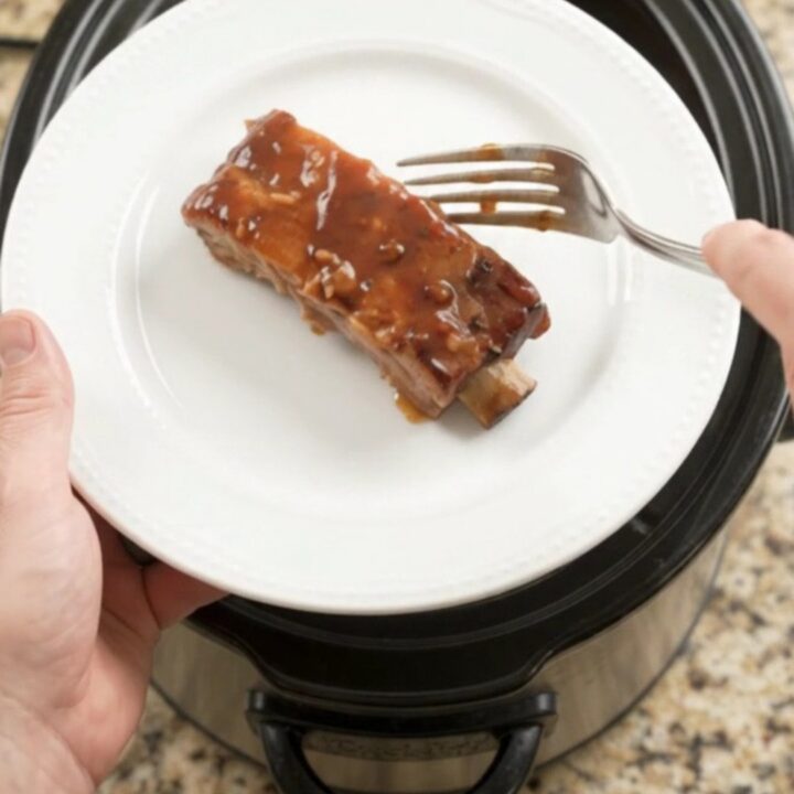 Glazed country-style pork ribs with apple slices in a slow cooker, topped with BBQ sauce.