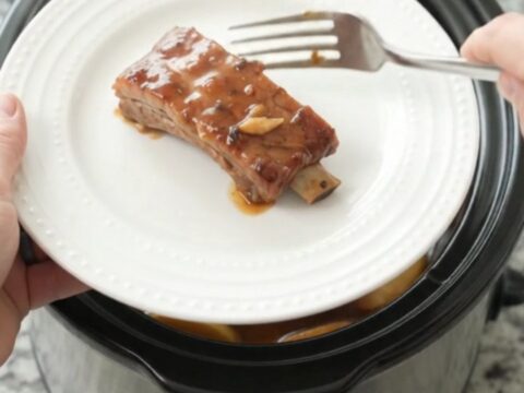 Slow cooker full of glazed pork ribs with soft apples and thick maple bourbon sauce