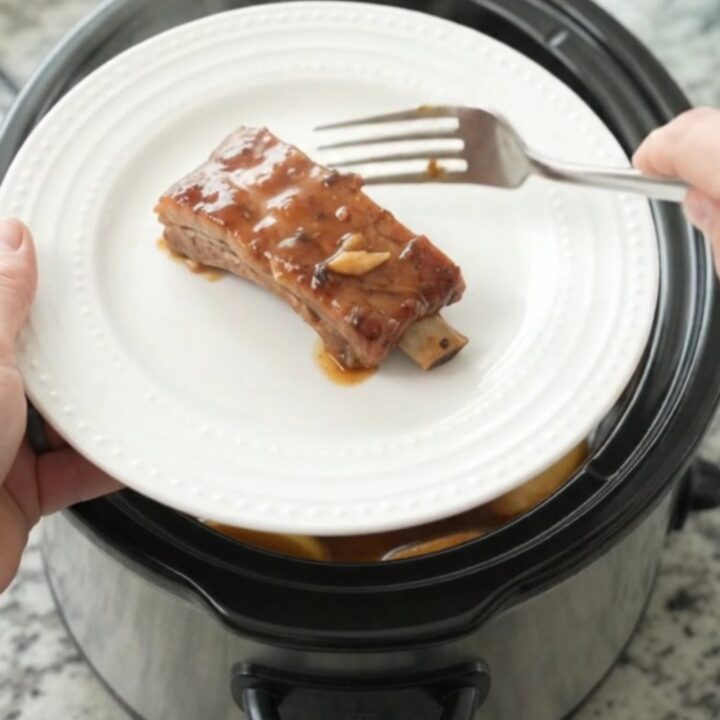 Slow cooker full of glazed pork ribs with soft apples and thick maple bourbon sauce