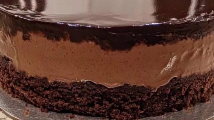A three-layer chocolate mousse cake with a glossy mirror glaze on a silver board.