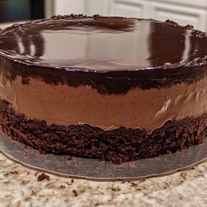 A three-layer chocolate mousse cake with a glossy mirror glaze on a silver board.