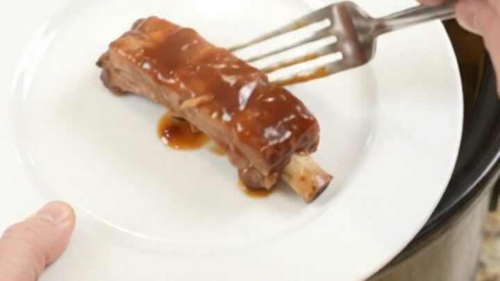 Slow cooker filled with glazed pork ribs, pineapple rings, and BBQ sauce