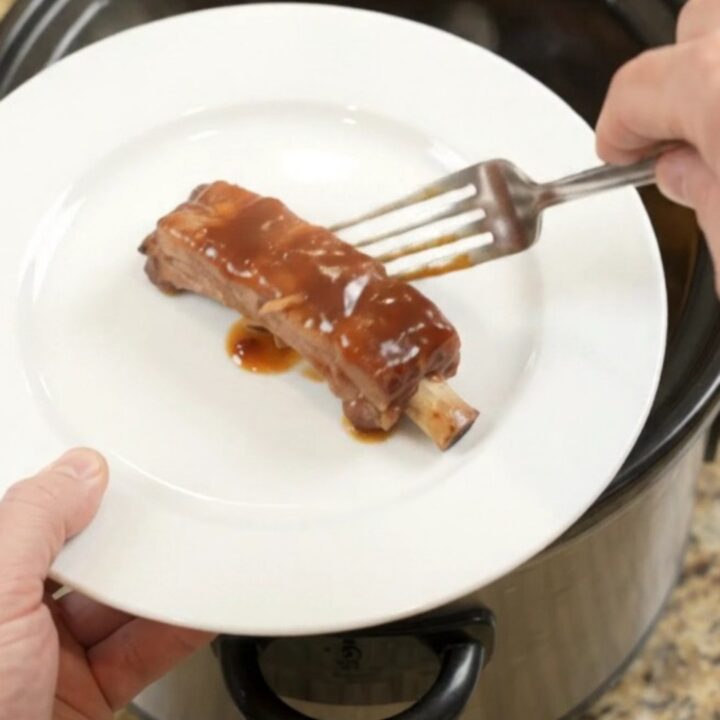 Slow cooker filled with glazed pork ribs, pineapple rings, and BBQ sauce