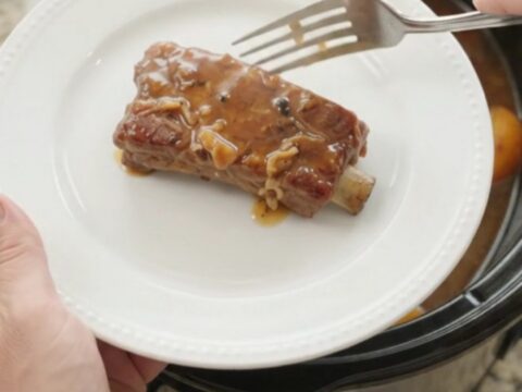 Tender country-style pork ribs glazed with peach bourbon BBQ sauce in a slow cooker, with sliced peaches