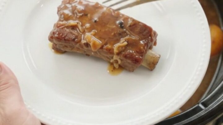 Tender country-style pork ribs glazed with peach bourbon BBQ sauce in a slow cooker, with sliced peaches