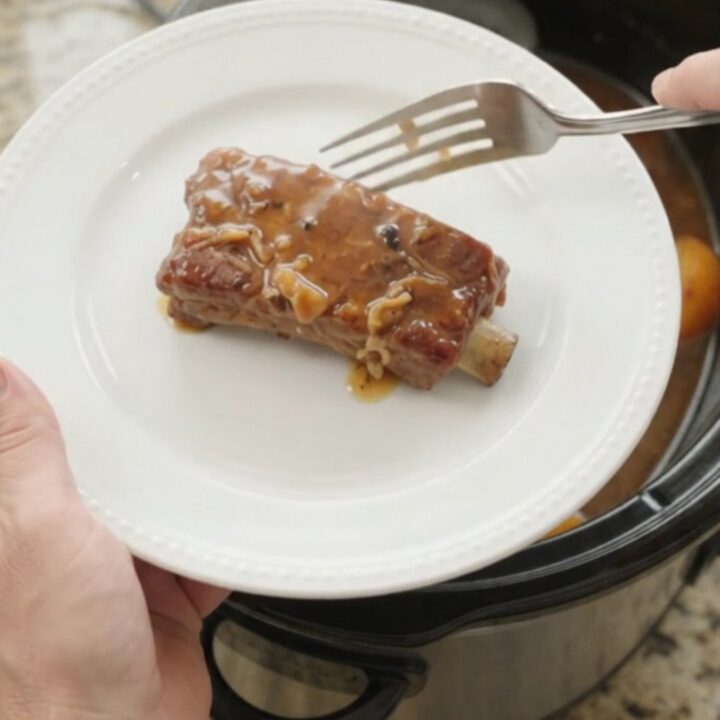 Tender country-style pork ribs glazed with peach bourbon BBQ sauce in a slow cooker, with sliced peaches