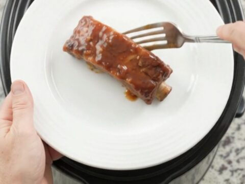 Slow cooker full of tender bourbon peach BBQ country ribs, glistening with sauce and caramelized peaches.