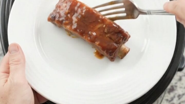 Slow cooker full of tender bourbon peach BBQ country ribs, glistening with sauce and caramelized peaches.