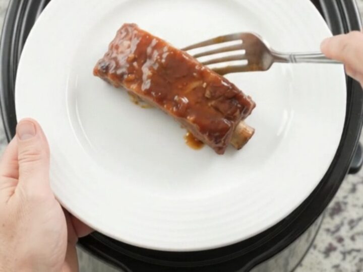 Slow cooker full of tender bourbon peach BBQ country ribs, glistening with sauce and caramelized peaches.