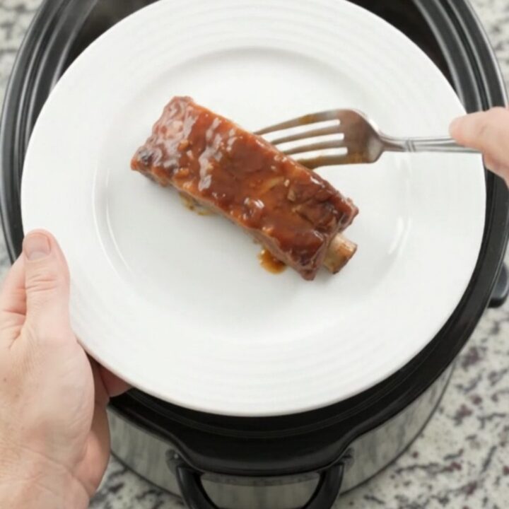 Slow cooker full of tender bourbon peach BBQ country ribs, glistening with sauce and caramelized peaches.