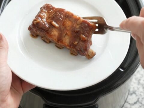 Slow cooker country pork ribs glazed with smoky chipotle honey barbecue sauce, garnished with fresh herbs on a white plate.
