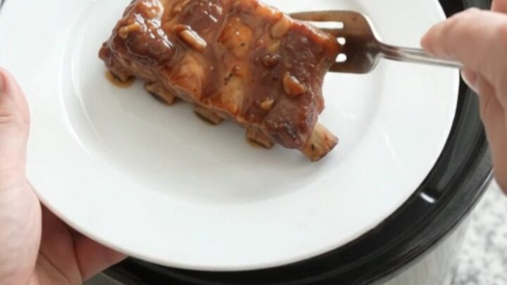 Slow cooker country pork ribs glazed with smoky chipotle honey barbecue sauce, garnished with fresh herbs on a white plate.