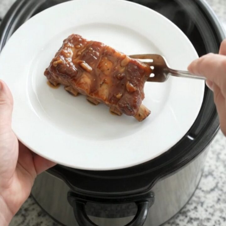 Slow cooker country pork ribs glazed with smoky chipotle honey barbecue sauce, garnished with fresh herbs on a white plate.