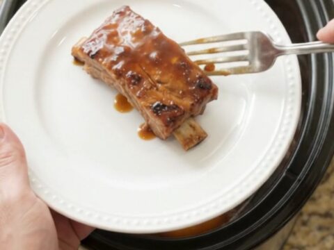 Slow cooker ribs with peaches and BBQ sauce, glistening and tender in a black crockpot