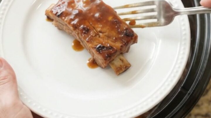 Slow cooker ribs with peaches and BBQ sauce, glistening and tender in a black crockpot