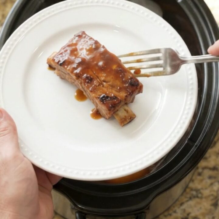 Slow cooker ribs with peaches and BBQ sauce, glistening and tender in a black crockpot