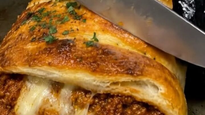 A golden, flaky braided pastry stuffed with savory ground beef and melted cheese, resting on a baking sheet.
