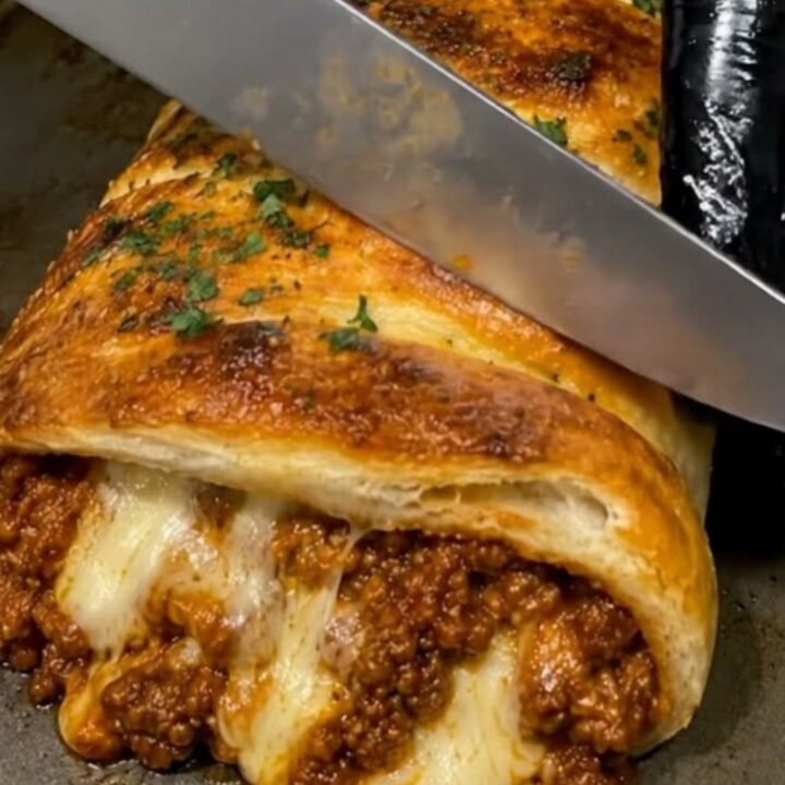 A golden, flaky braided pastry stuffed with savory ground beef and melted cheese, resting on a baking sheet.