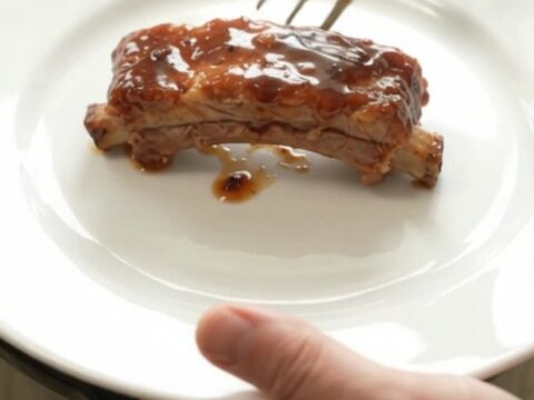 Slow cooker bourbon peach pork ribs in a black crockpot with glossy sauce and peach slices.