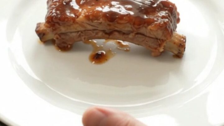 Slow cooker bourbon peach pork ribs in a black crockpot with glossy sauce and peach slices.
