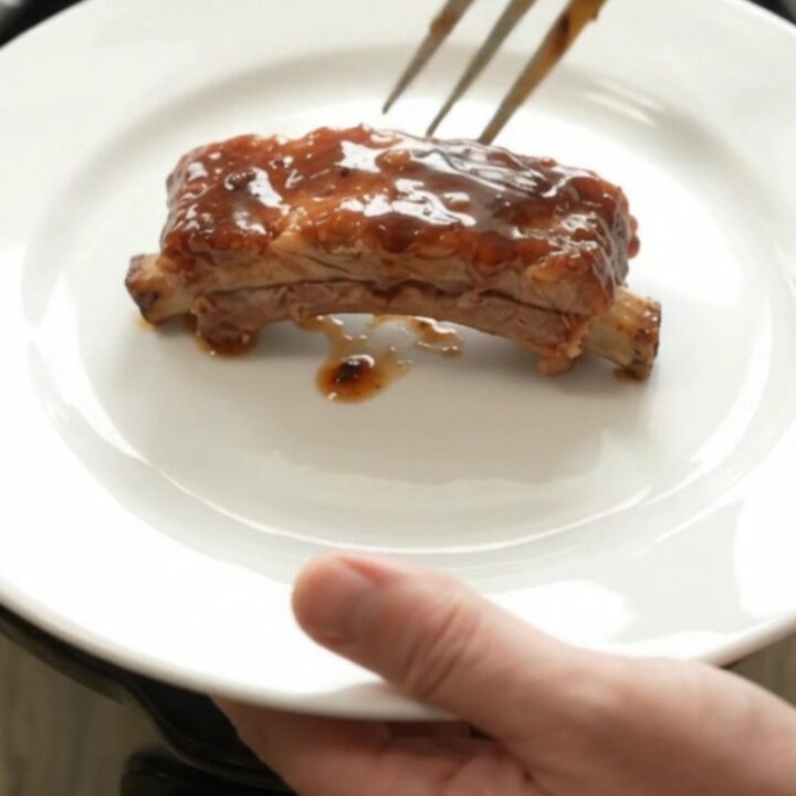 Slow cooker bourbon peach pork ribs in a black crockpot with glossy sauce and peach slices.