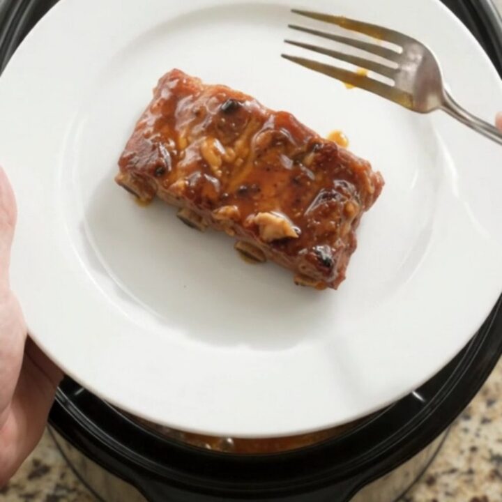 A slow cooker filled with glossy, fork-tender country-style pork ribs coated in a dark