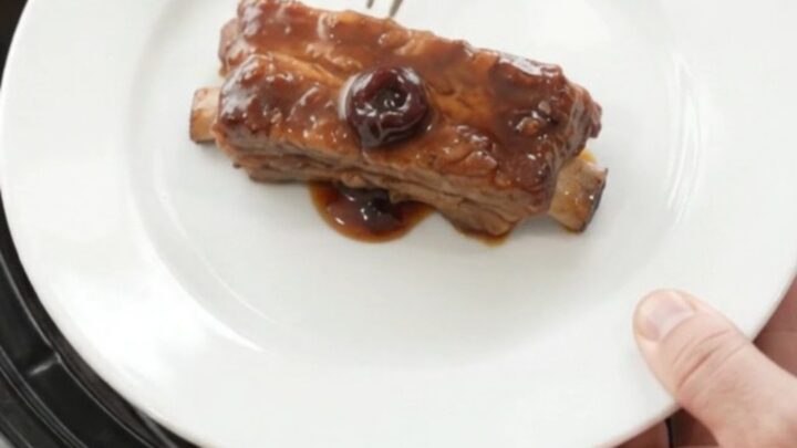 Cherry cola molasses country pork ribs in a slow cooker, glistening with dark sauce and cherries.