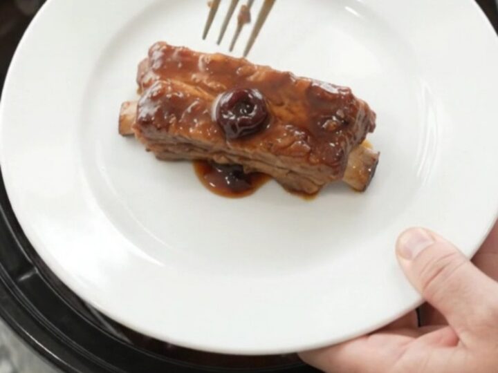Cherry cola molasses country pork ribs in a slow cooker, glistening with dark sauce and cherries.