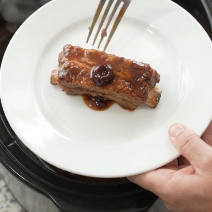 Cherry cola molasses country pork ribs in a slow cooker, glistening with dark sauce and cherries.