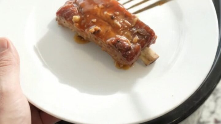 Slow cooker filled with glazed pork ribs in maple bourbon sauce, topped with garlic and rosemary.