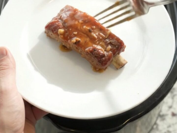 Slow cooker filled with glazed pork ribs in maple bourbon sauce, topped with garlic and rosemary.