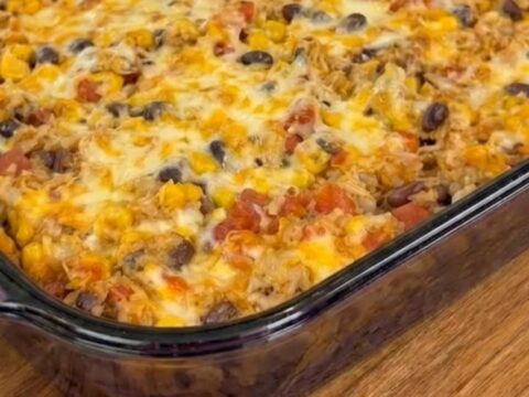 A spatula scooping into a golden, bubbly cheesy chicken burrito casserole in a glass baking dish.