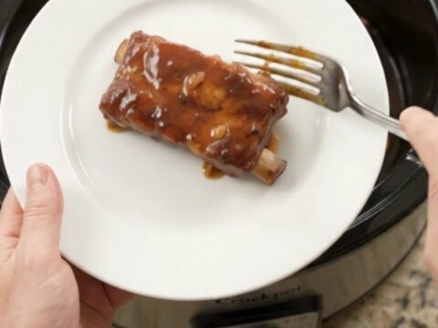 Slow cooker country-style pork ribs glazed with honey hickory BBQ sauce, topped with garlic cloves and rosemary